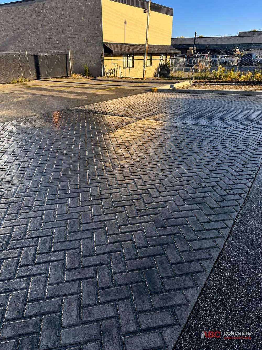 Large commercial parking area finished in a charcoal herringbone stamped brick pattern