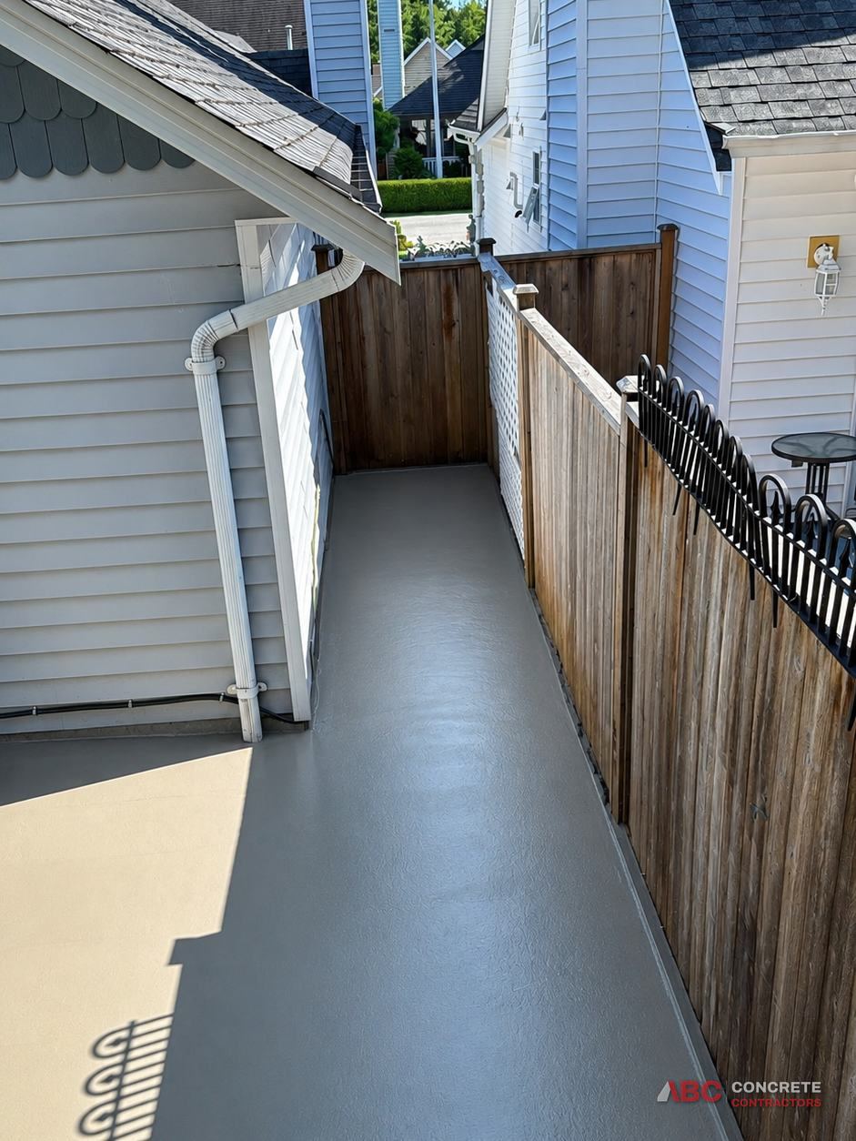 Side yard walkway coated in grey and sand tones running between a house and a cedar fence
