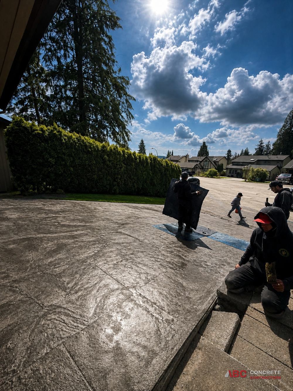 ABC Concrete crew laying stamp mats into a fresh driveway pour on a sunny day in Metro Vancouver